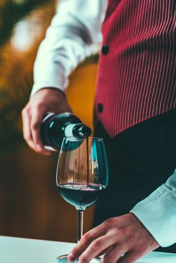 A sommelier pouring red wine into a stemmed glass